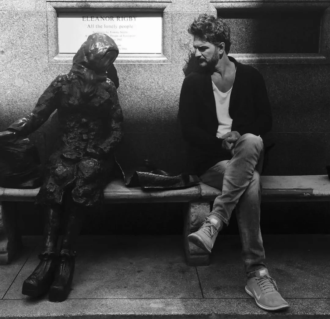 Ricardo Arjona sentado junto a una escultura