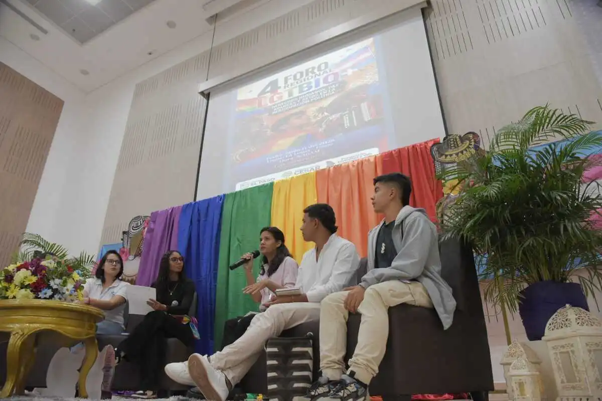 En el Mes del Orgullo LGBTIQ+, el Cesar afianza su agenda de derechos, paz y participación política con la realización del Cuarto Foro Regional LGBTIQ+ en La Loma (El Paso), el 11 de junio, y la preparación de la marcha del Orgullo que se llevará a cabo en Valledupar el próximo 28 de junio. El Cuarto Foro Regional “Derechos humanos, paz, avances y retos en la participación política” fue liderado por el defensor de derechos humanos Rafael Jiménez, director de la Fundación Diversidad y Vida y referente del movimiento LGBTIQ+ en el Cesar. El foro se desarrolló en el marco de la Semana de la Diversidad. Política pública y recursos: un hito para el departamento Durante el encuentro, el jefe de la Oficina de Política Social de la Gobernación del Cesar, Juan Carlos Mindiola, resaltó que el departamento cuenta por primera vez con una política pública integral LGBTIQ+ con horizonte a 15 años, construida de manera participativa con organizaciones de todo el territorio. “Por primera vez en la historia del Cesar ustedes plasmaron en una política pública sus derechos, y eso es aplaudible”, afirmó el funcionario, quien recordó que este proceso fue reconocido por el Ministerio del Interior como una de las mejores políticas integrales del país. Mindiola subrayó que la administración departamental respaldará la implementación con recursos anuales. “Ya estamos en la construcción del plan de acción y contamos con 2.800 millones de pesos cada año para desarrollar esta política pública, con acciones afirmativas en educación, salud, deporte, cultura, vivienda y otros ámbitos que la población requiera”, explicó. El papel de la población diversa en la paz territorial Uno de los ejes centrales del foro fue el papel de las personas LGBTIQ+ en la construcción de paz, la reconciliación y la transformación de territorios históricamente afectados por el conflicto armado. Desde Caribe Afirmativo se recordó que, durante la guerra, en departamentos como el Cesar era prácticamente imposible que las personas LGBTIQ+ se organizaran abiertamente, lo que retrasó el movimiento en comparación con otros sectores sociales. “El acuerdo de paz abrió la posibilidad de encontrarnos, hablar de nuestras vivencias y organizarnos. Eso ha permitido fortalecer liderazgos y promover el reconocimiento de derechos en el territorio”, expusieron sus representantes. Jason Sarmiento, presidente del Consejo Departamental de Juventudes y líder del proceso de reincorporación en Tierra Grata, enfatizó en la incidencia política de la población diversa. “Uno de los grandes avances es que hoy la diversidad sexual tiene la oportunidad de participar en distintos escenarios y ejercer liderazgo. El rol fundamental en la construcción de paz es la reconciliación”, afirmó. “Durante años se dijo que la antigua guerrilla discriminaba y atacaba a la población diversa; hoy vemos organizaciones donde conviven firmantes de paz, mujeres, jóvenes y personas LGBTIQ+ construyendo tejido social, educación y participación desde los territorios”, añadió. Barreras que persisten: estigmas, miedo y vacíos institucionales Aunque los participantes reconocieron avances significativos en organización social y normatividad, coincidieron en que persisten barreras profundas, tanto sociales como institucionales. Entre las barreras más mencionadas se encuentran: Estigmatización y lenguaje discriminatorio que se reproduce en calles, hogares y escenarios comunitarios. Autocensura política por miedo a agresiones, burlas o señalamientos cuando se participa en espacios de decisión. Falta de protocolos de atención con enfoque diferencial en instituciones públicas. Vacíos en la tipificación de violencias basadas en género contra personas LGBTIQ+, particularmente contra mujeres trans. “Muchas veces, cuando una mujer trans denuncia violencia en el ámbito íntimo, no se reconoce como violencia de género ni como violencia intrafamiliar, sino como una simple agresión personal”, explicaron voceras de Caribe Afirmativo. “Eso termina en conciliaciones que no garantizan su seguridad, y cuando ocurre un homicidio, raramente se reconoce como feminicidio o transfeminicidio”. Desde el trabajo con víctimas y organizaciones, se insistió en que Colombia necesita avanzar en el reconocimiento jurídico de las violencias específicas que enfrentan las personas LGBTIQ+, y que la protección no puede descansar solo en leyes generales que no recogen estas realidades. La apuesta por las nuevas generaciones Las experiencias personales compartidas durante el foro evidenciaron cambios, pero también deudas. Eric González, joven trans que marcó un hito en el sistema educativo del Cesar, narró su tránsito por el colegio: “Poder portar el uniforme masculino y culminar el bachillerato con mi nombre identitario fue un proceso complejo, pero necesario. Para quienes vienen detrás, la política pública y estos debates van a abrir caminos que antes no existían”, expresó. González insistió en que aún falta empatía y acompañamiento, pero valoró el rol de las organizaciones y de instituciones como el SENA en abrir rutas de formación con enfoque diferencial: “La participación ciudadana no está vacía; los espacios existen, pero hay que accionar las rutas y llenarlas con nuestras historias”. Desde la administración municipal de El Paso, se destacó que este es uno de los municipios con mayor número de jóvenes LGBTIQ+ inscritos en programas técnicos, tecnológicos y universitarios, gracias a esfuerzos de focalización y acceso a la educación superior. Para los líderes presentes, este es un avance concreto en la superación de la exclusión y la precarización histórica. El foro también sirvió para mostrar el crecimiento organizativo en el Cesar. Según los líderes del proceso, el departamento pasó de tener tres organizaciones LGBTIQ+ a más de 20, con presencia en distintas subregiones, incluyendo municipios del sur históricamente marginados. Agenda del Orgullo Las reflexiones del foro se articulan con la agenda del Mes del Orgullo en el departamento. Como evento central, la marcha del Orgullo LGBTIQ+ se realizará en Valledupar el próximo 28 de junio, acompañada de actividades culturales, pedagógicas y comunitarias en distintos municipios del Cesar, impulsadas por organizaciones sociales, la Gobernación y administraciones locales. Para sus organizadores, el foro en La Loma y la marcha en la capital del departamento son dos caras de una misma apuesta: convertir al Cesar en un territorio que avance de la política escrita a la vida cotidiana, donde la diversidad no sea motivo de violencia ni de exclusión, sino parte activa de la construcción de paz y democracia.