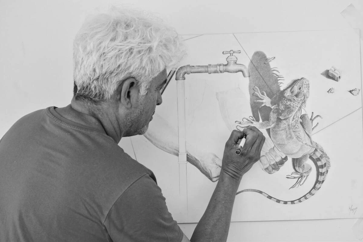 Carlos Meneses Rueda con el boceto en el que una iguana, una llave y un hombre lavándose las manos comparten el mismo espacio, jugando con la ambigüedad y la fuerza del blanco y negro. Foto: Said Armenta.